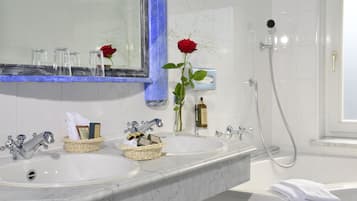 A bathroom with two sinks, a mirror, a shower, and a vase with a rose.