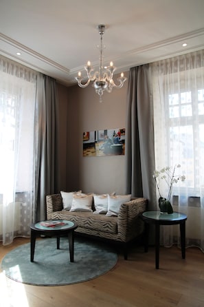 A living room with a sofa, two side tables, a chandelier, and a painting on the wall. - Hotel Torbräu (Munich)