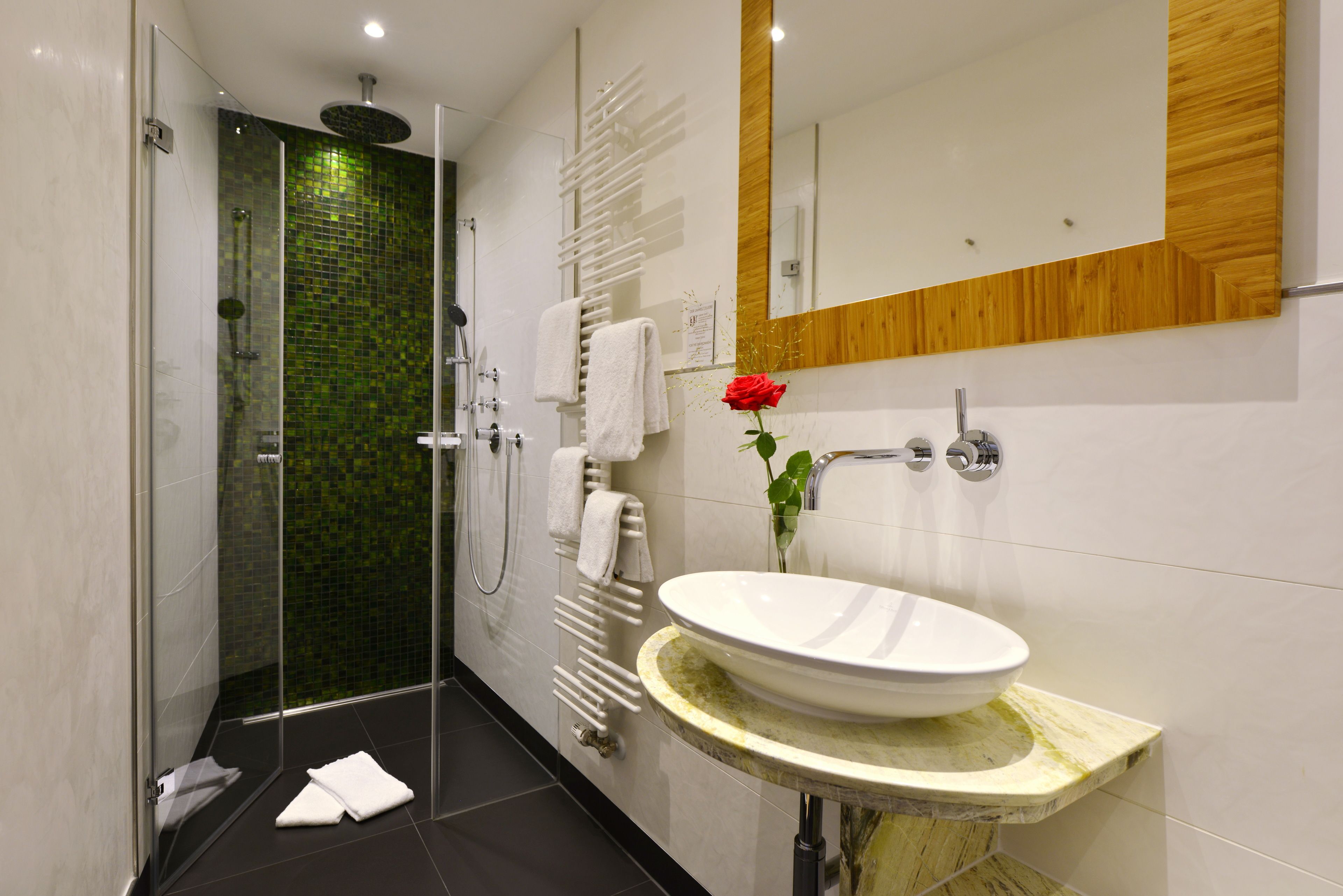 A modern bathroom with a glass-enclosed shower, a white sink with a marble countertop, and a wooden panel above the mirror.
