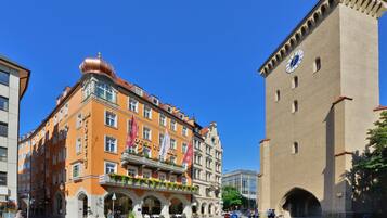 A historic building with a clock tower, a hotel with a red facade, and a cobblestone plaza.
