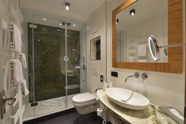 A modern bathroom with a glass-enclosed shower, a white toilet, and a large sink with a mirror above it.
