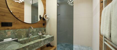 A modern bathroom with a wooden vanity, a glass shower enclosure, and a round mirror.