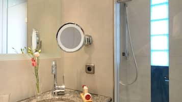 Une salle de bain moderne avec un lavabo surmonté d’un plan de travail en granit, un miroir rond et une douche à parois de verre.