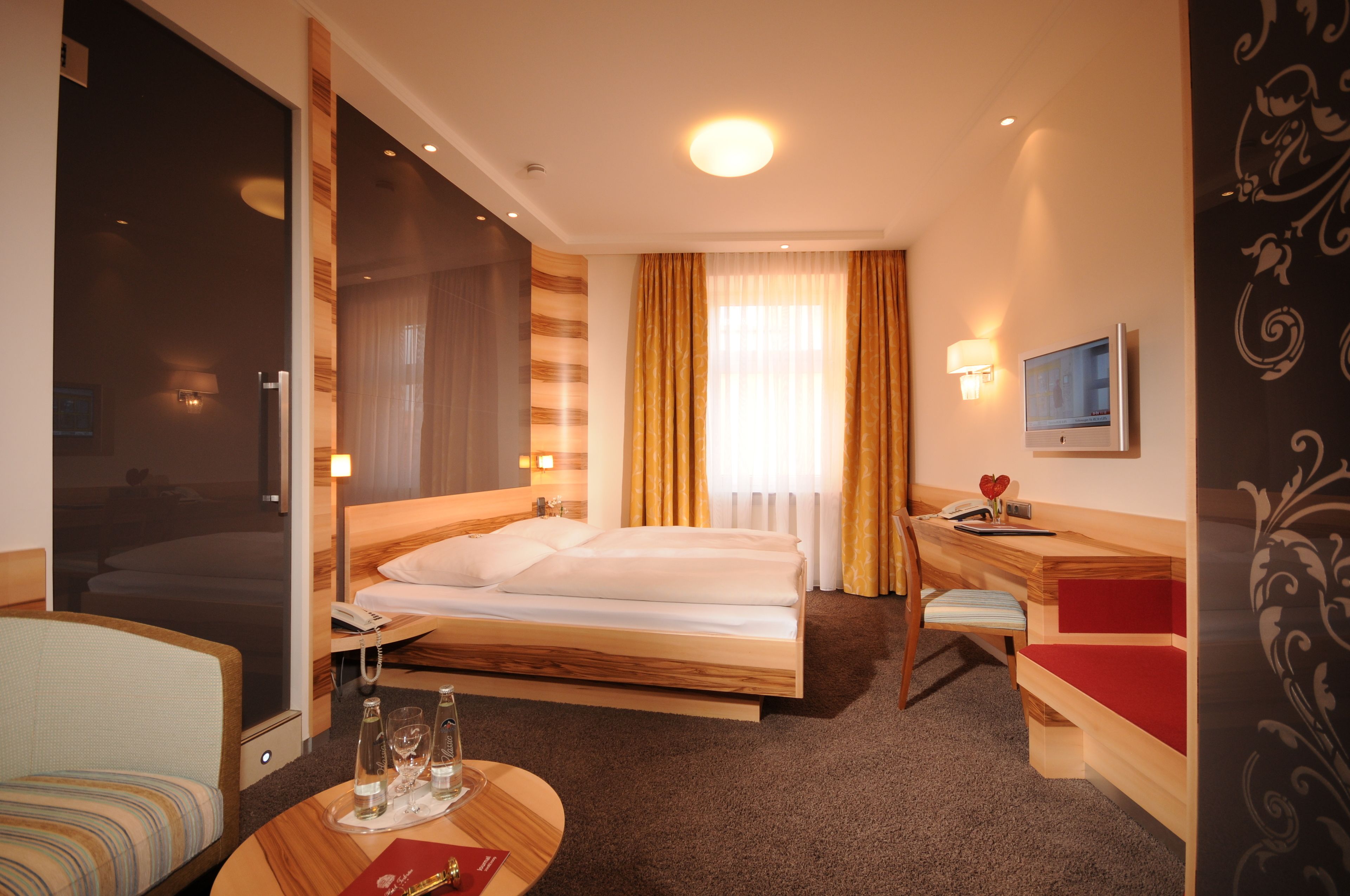 Una habitación de hotel con cama, escritorio, silla, televisor y ventana con cortinas.