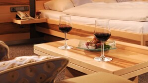 Hotellihuone, jossa on sänky, yöpöytälamput, yöpöytä, jossa on viinilasi ja hedelmävati, sekä tuoli.