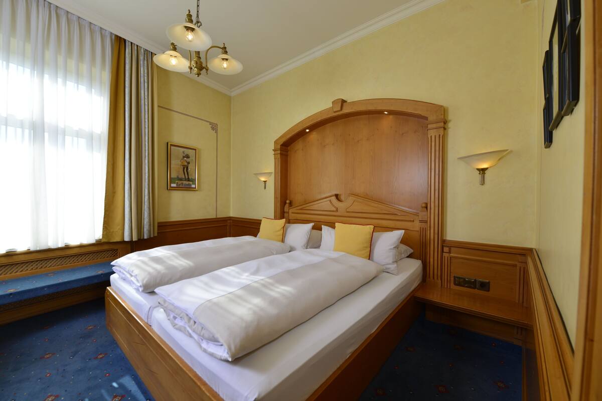 Una cama doble con ropa de cama blanca, un cabecero de madera y dos mesitas de noche con lámparas.