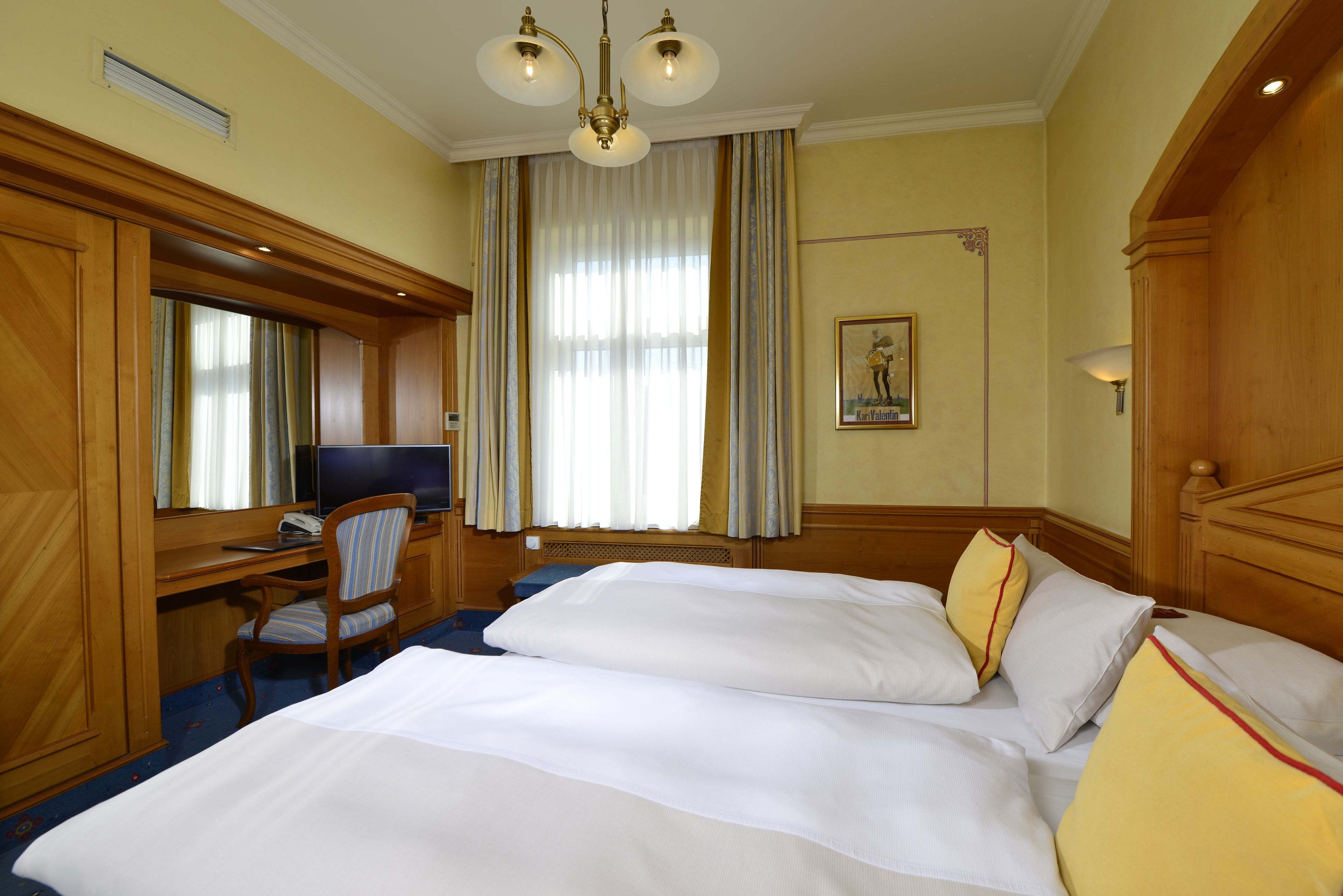 A hotel room with two beds, a desk with a chair, a television, and a large window with curtains.
