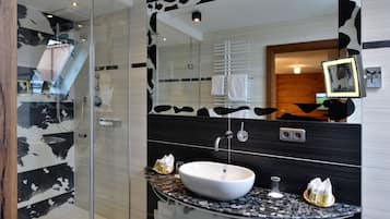 Ein modernes Badezimmer mit einer gläsernen Duschkabine, einem weißen Waschbecken und einem Spiegel mit Kuhmuster.