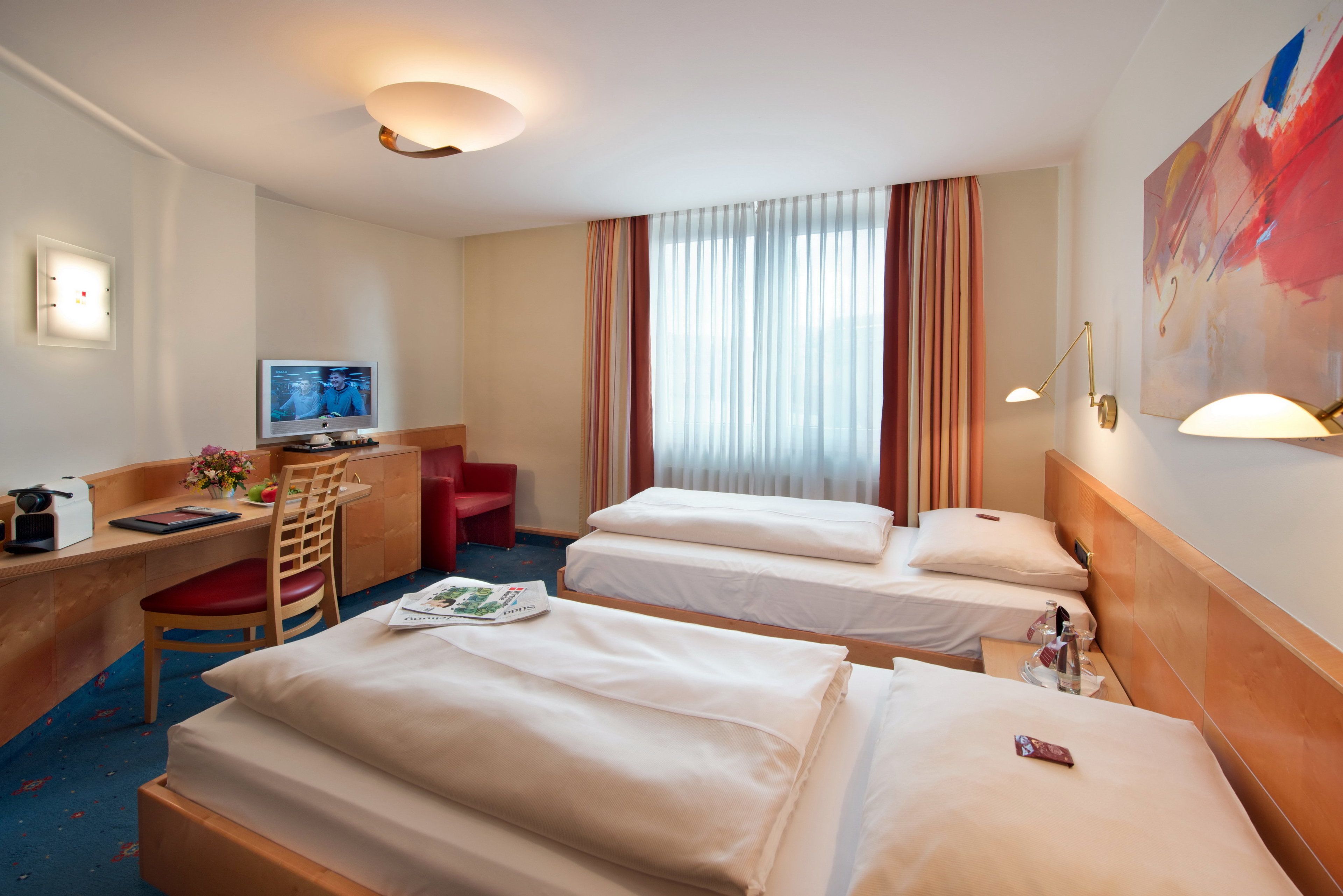 Quarto de hotel com duas camas, uma escrivaninha com computador, uma cadeira e uma televisão.