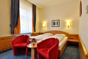 Ein Hotelzimmer mit einem Bett, zwei roten Sesseln, einem kleinen Tisch und zwei Wandleuchten.