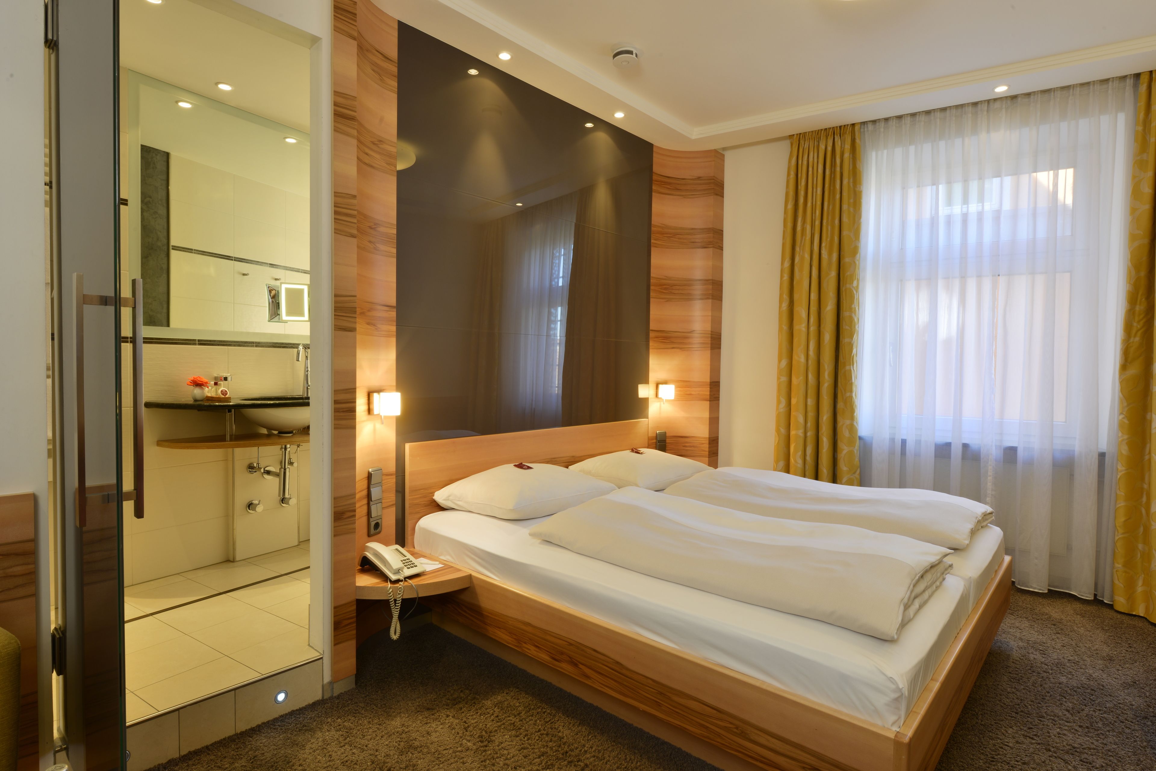 A hotel room with a large bed, a bedside table with a phone, a mirror, and a shower area.