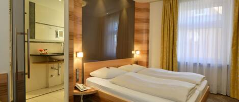 A hotel room with a large bed, a bedside table with a phone, a mirror, and a shower area.