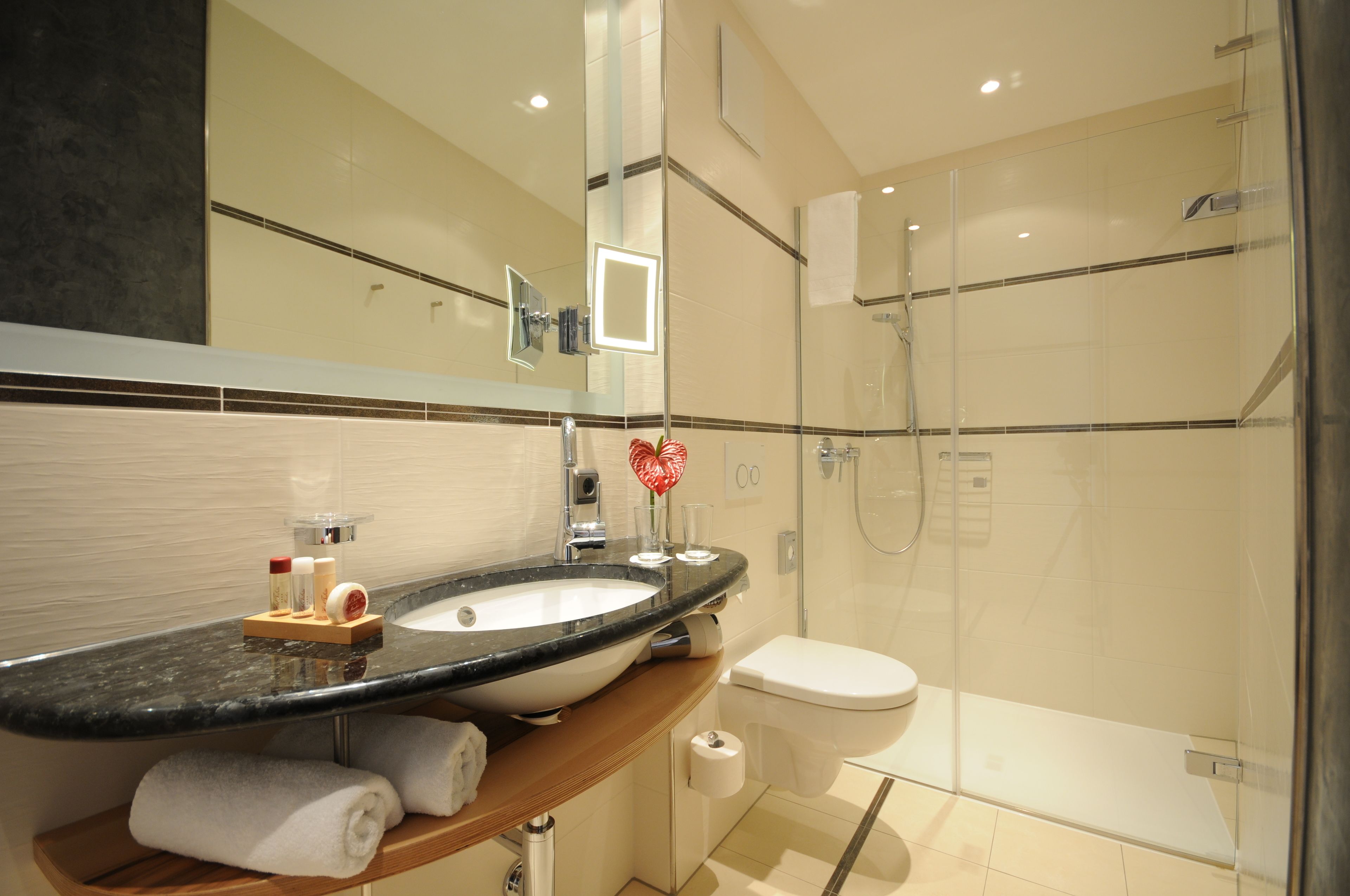 A modern bathroom with a large mirror, a sink, a toilet, and a glass-enclosed shower.