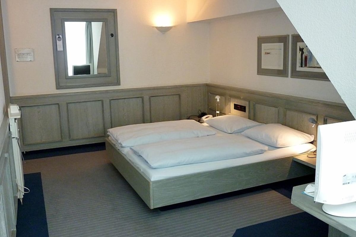 A hotel room with a large bed, bedside tables, a mirror, and a wall-mounted light.