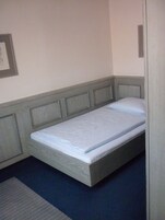 Una cama individual con cabecera de madera y colchón azul en una habitación con paredes lisas y suelo oscuro.