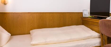 Una cama individual con cabecera de madera, una mesita de noche con televisor de pantalla plana y una silla con asiento de mimbre.