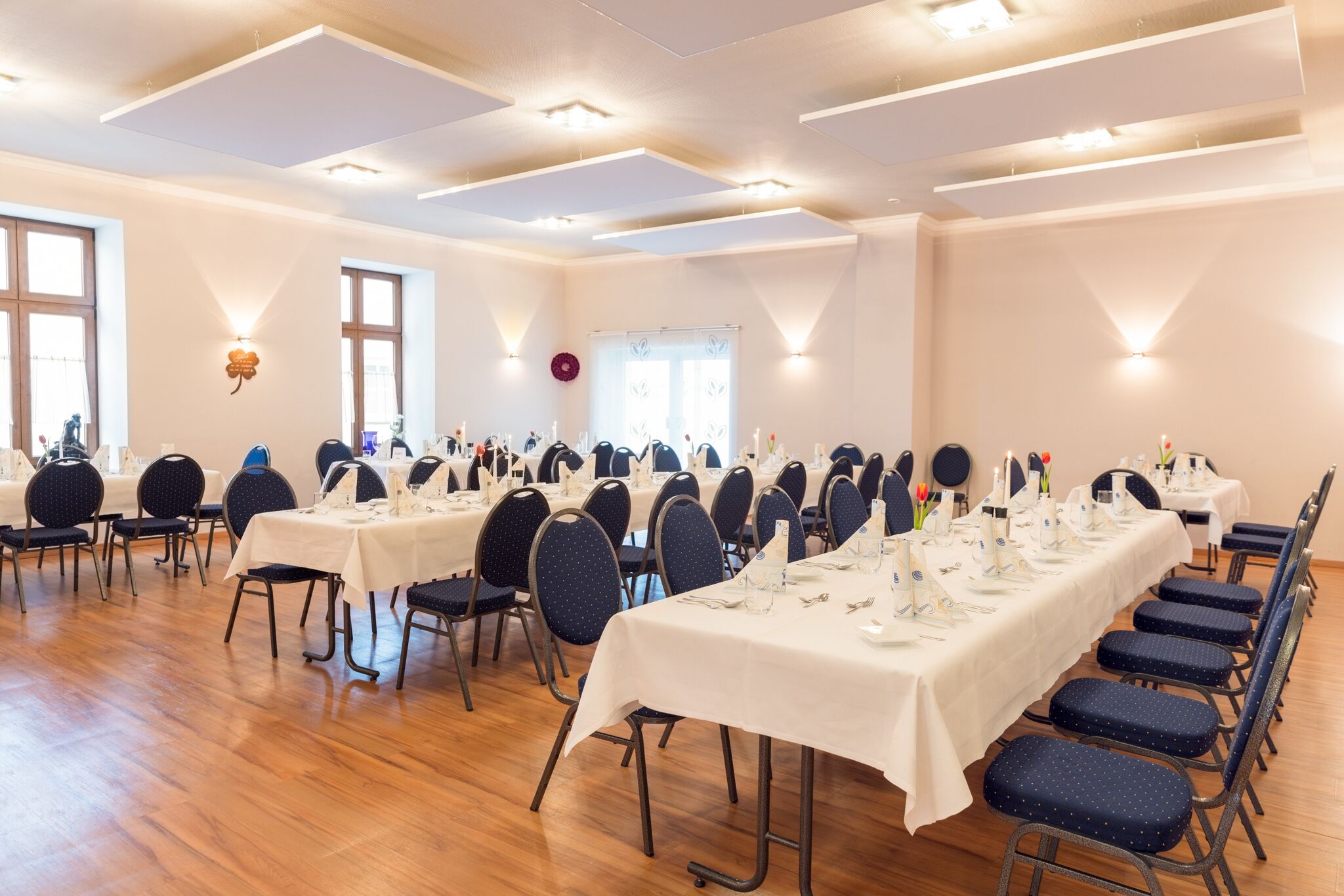 Ein Konferenzraum mit mehreren Tischen, gedeckt für eine Mahlzeit, ausgestattet mit Stühlen und Tischdekoration.