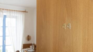 Una porta de fusta amb el número 44, una finestra amb cortines lleugeres, i un interior borrat amb una taula i una cadira.