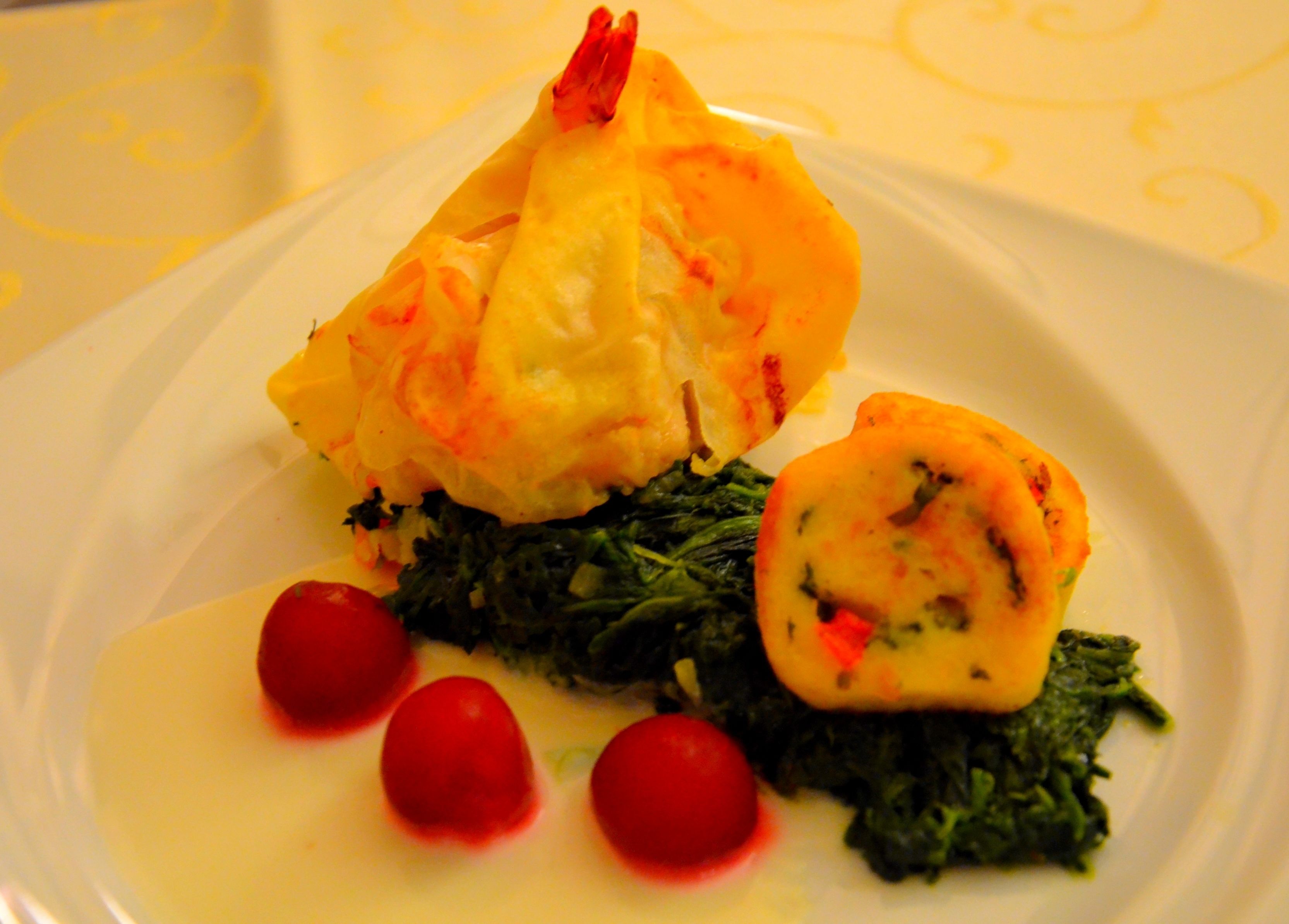 A plate with a stuffed chicken breast, a rolled vegetable, and some greens with cherry tomatoes.