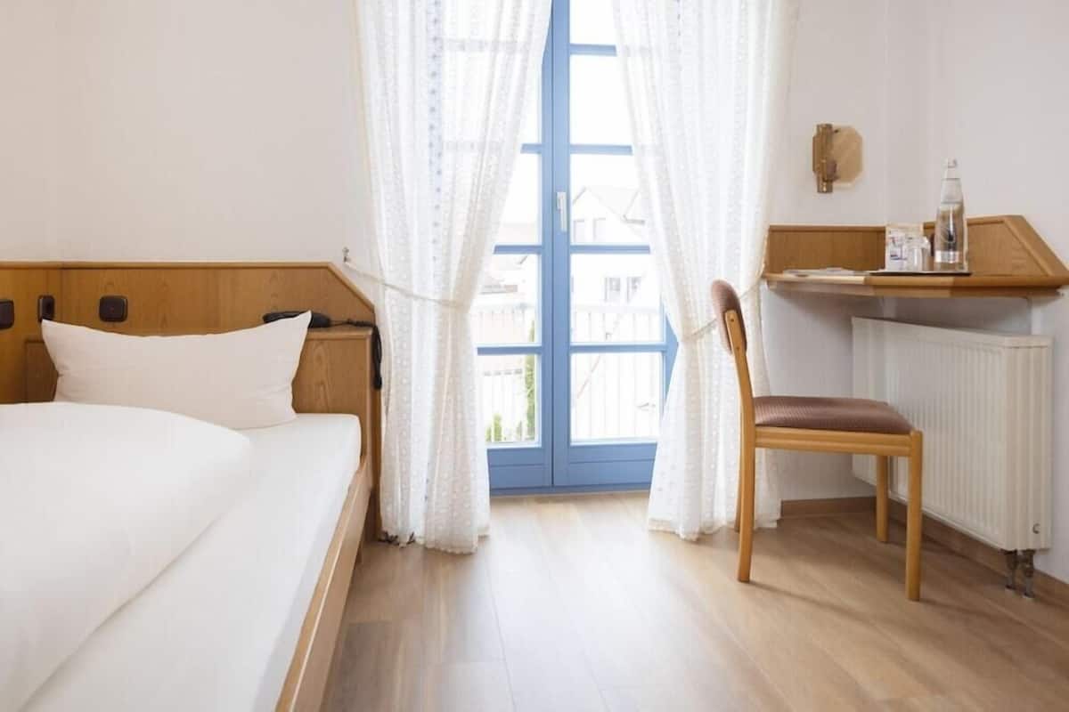 Un dormitorio con una cama, una silla, un escritorio y una ventana con cortinas.