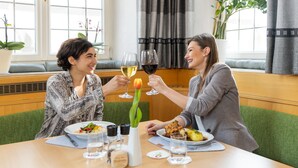 Two people sitting at a table with plates of food, glasses of wine, and a vase with a tulip.