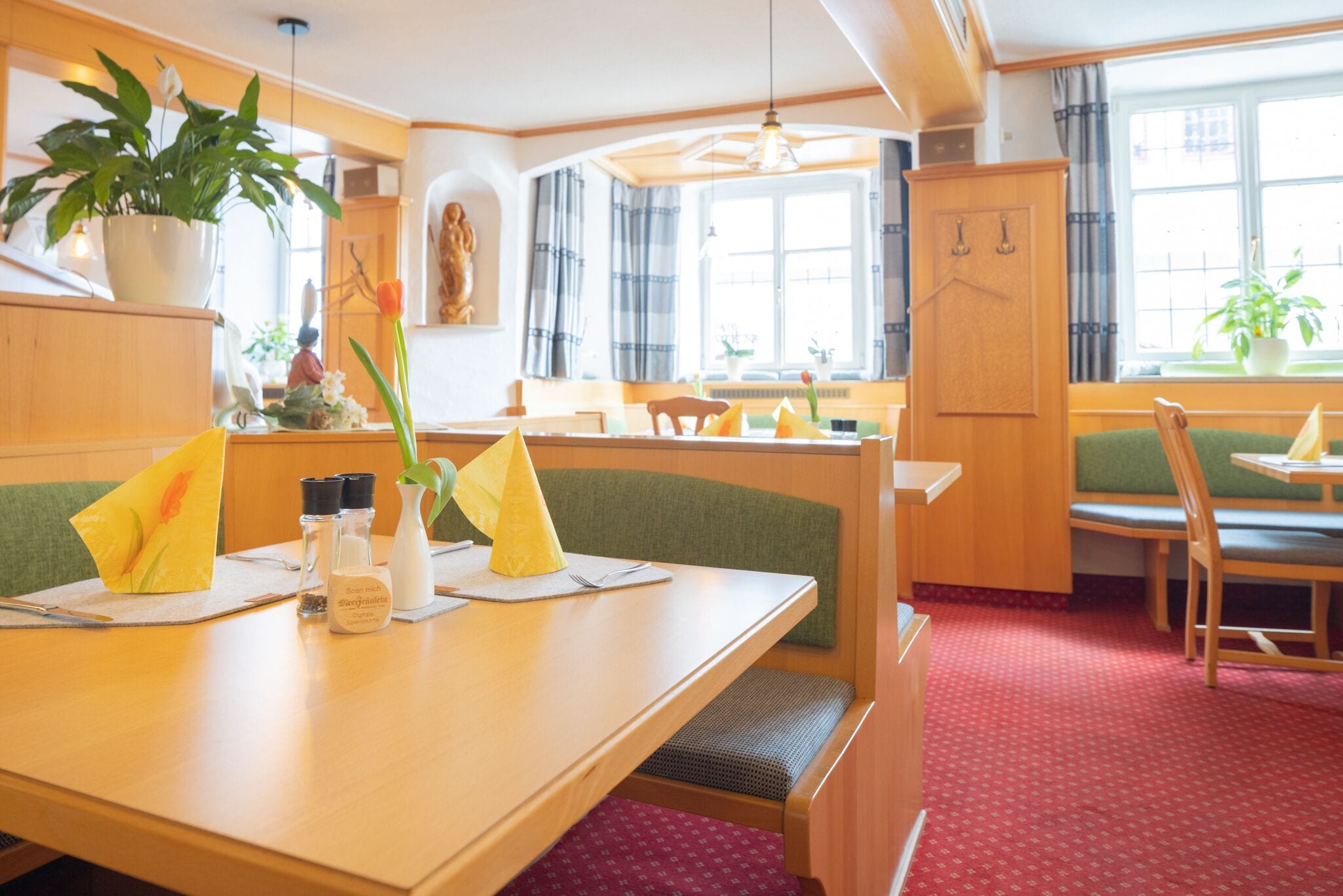 Un restaurante con mobiliario de madera, asientos acolchados color verde y plantas en macetas.