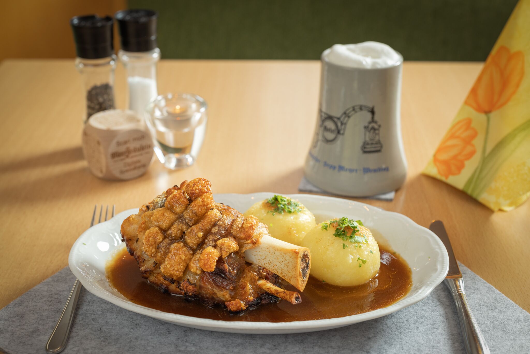 Prato com joelho de porco assado, molho e batatas cozidas.