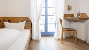 A bedroom with a bed, a chair, a window with curtains, a wooden headboard, a bedside table, and a radiator.