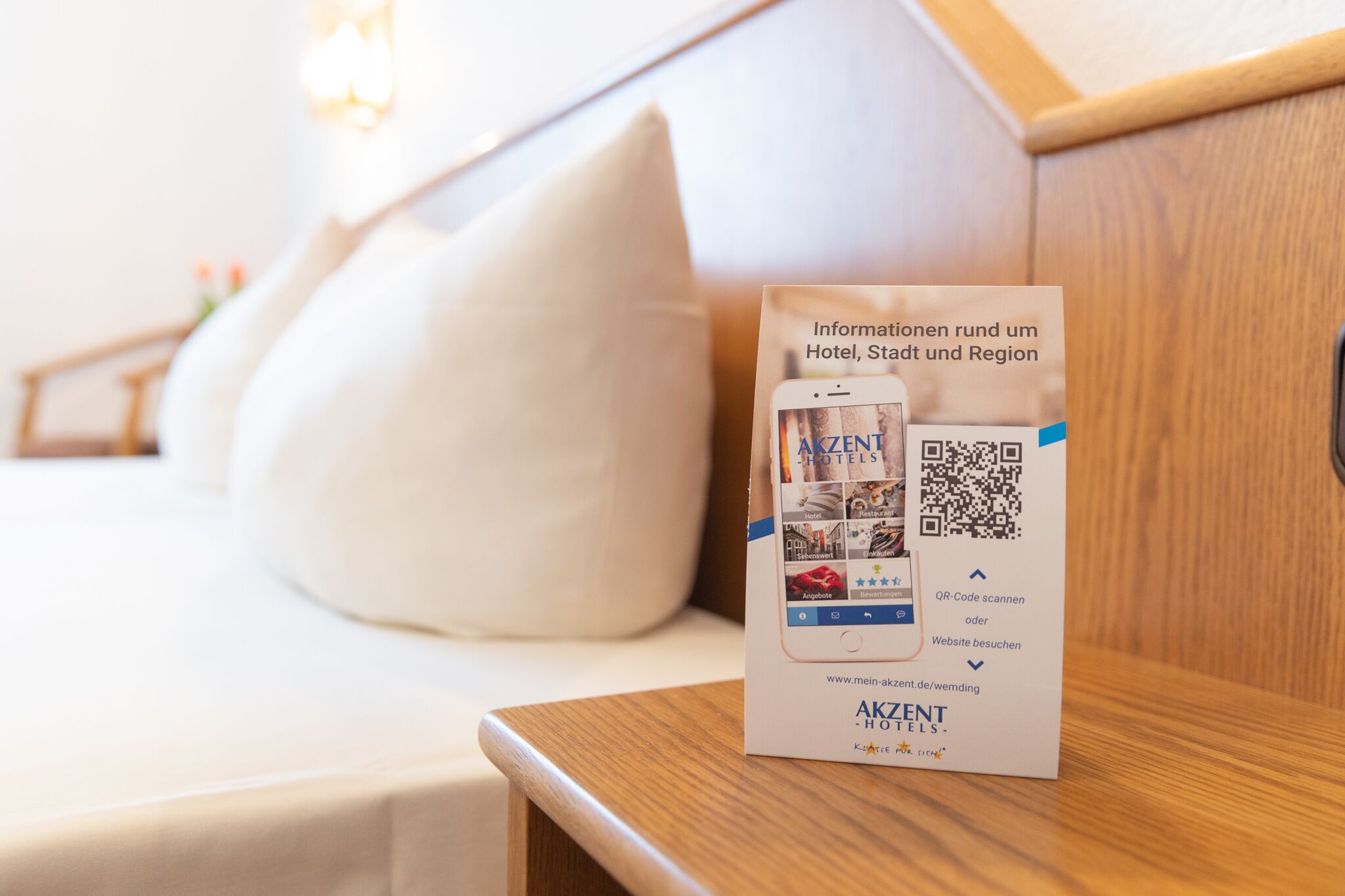 Eine Broschüre auf einem Holztisch mit einem QR-Code und einer Website-Verlinkung für AKZENT Hotels.