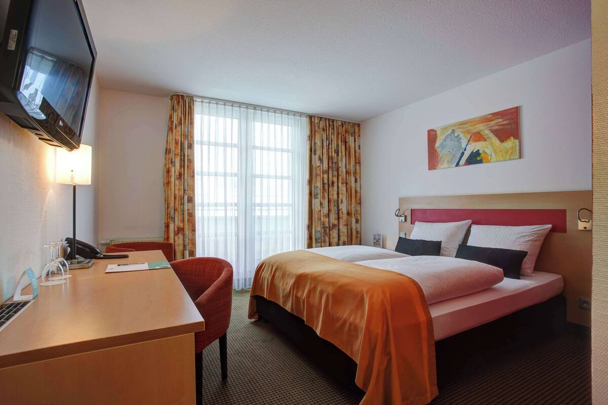 A hotel room with a bed, a desk, a chair, a television, and a window with curtains.
