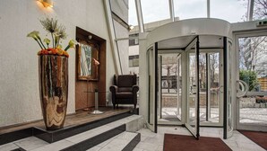 Un vestíbulo de hotel con un jarrón grande de flores, una silla y una puerta giratoria.