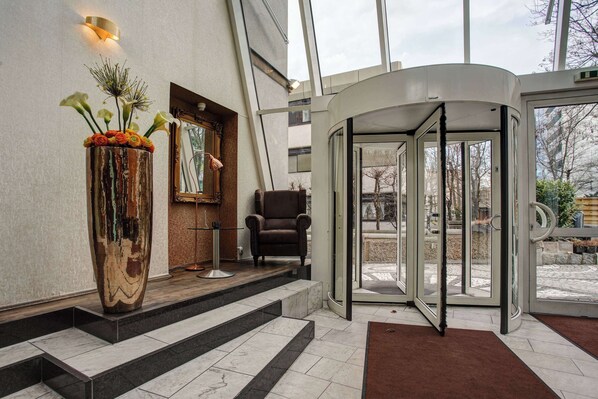 Un vestíbulo de hotel con un jarrón grande de flores, una silla y una puerta giratoria.