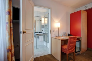 Habitación de hotel con escritorio, silla y baño visible a través de una puerta abierta.