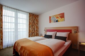 Una habitación de hotel con una cama grande, un cuadro en la pared y una ventana con cortinas.