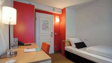 Habitación de hotel con escritorio, cama, silla, lámpara y luz en la pared.