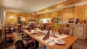 Un comedor de hotel con mobiliario de madera, varias mesas y una cocina al fondo.