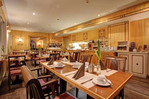 A hotel dining area with wooden furniture, multiple dining tables, and a kitchen in the background.