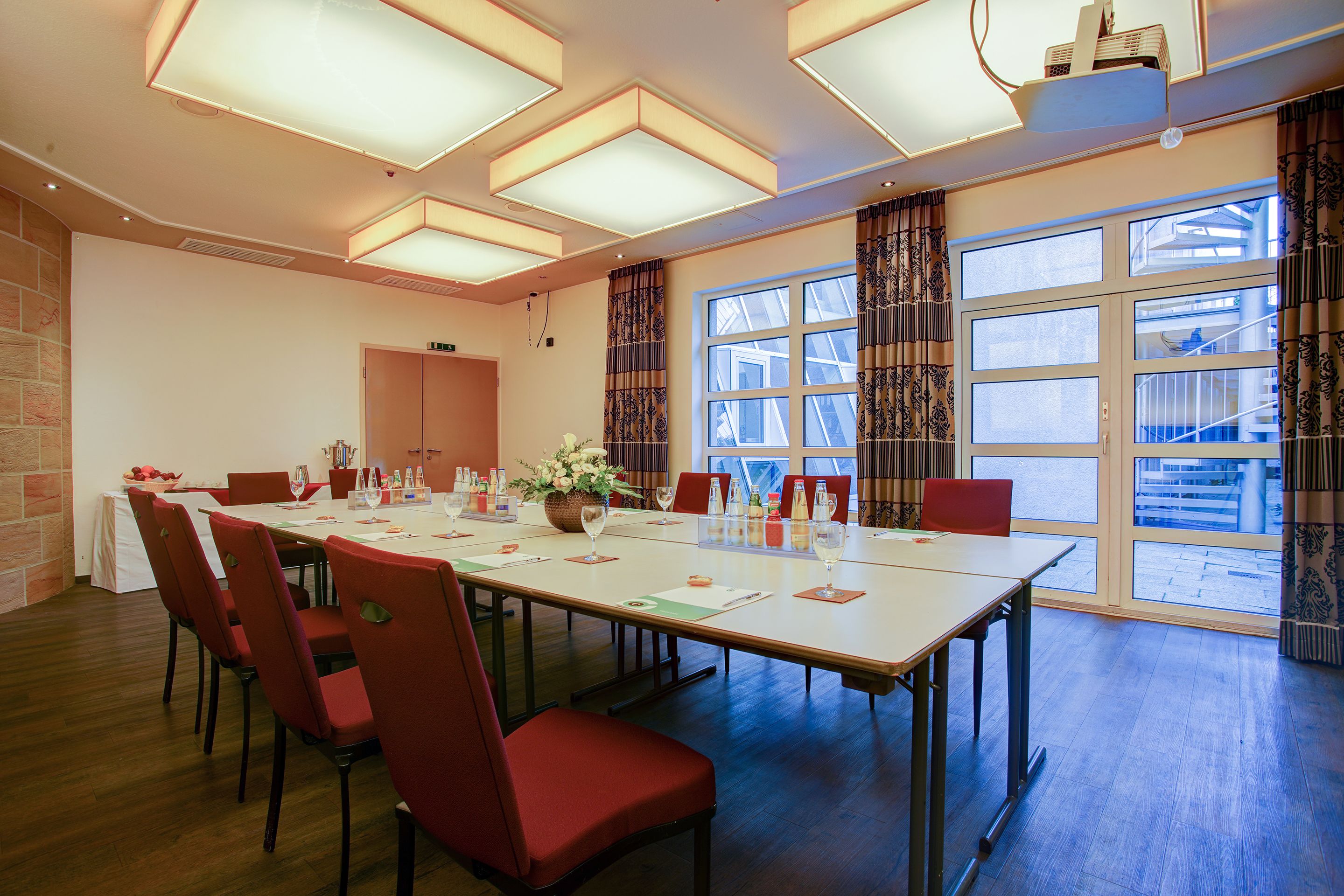 Ein Konferenzraum mit langem Tisch, roten Stühlen und einem großen Fenster mit Vorhängen.