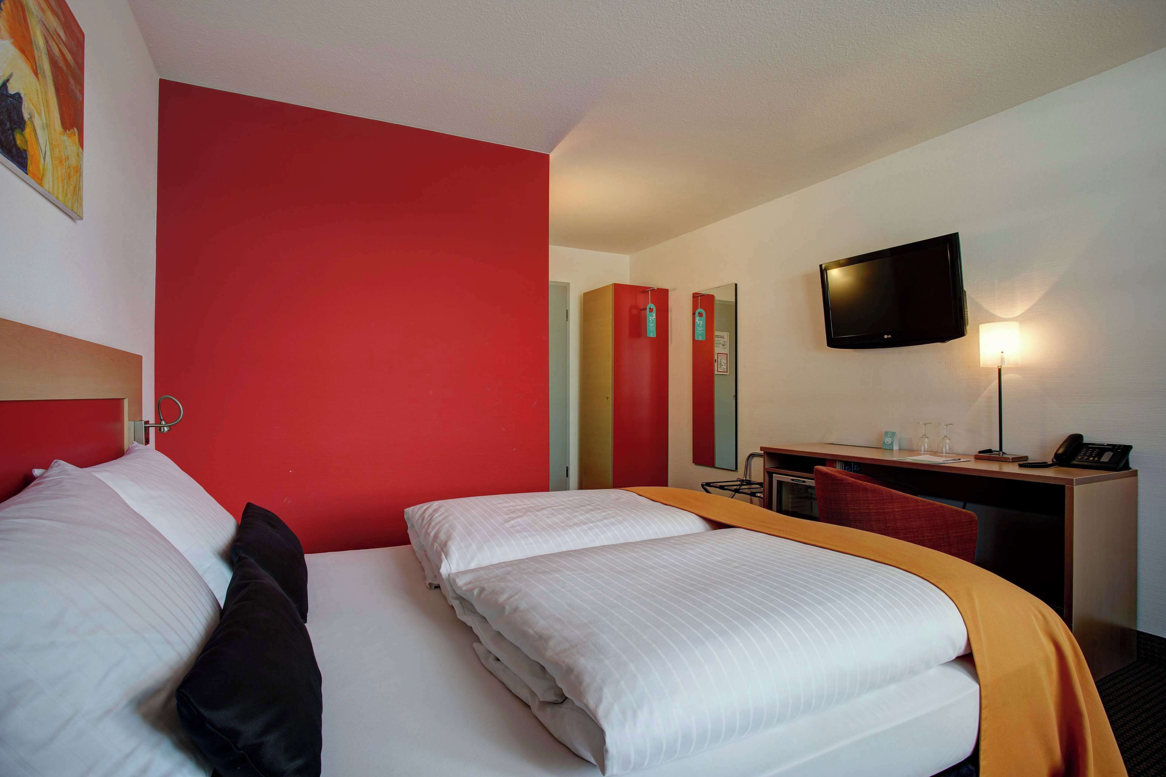 Ein Hotelzimmer mit zwei Betten, einem Schreibtisch, einem Stuhl, einem Fernseher und einer Lampe.