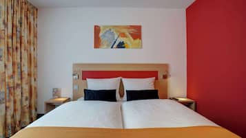 A hotel room with a bed, two nightstands, a red accent wall, and a painting above the bed.