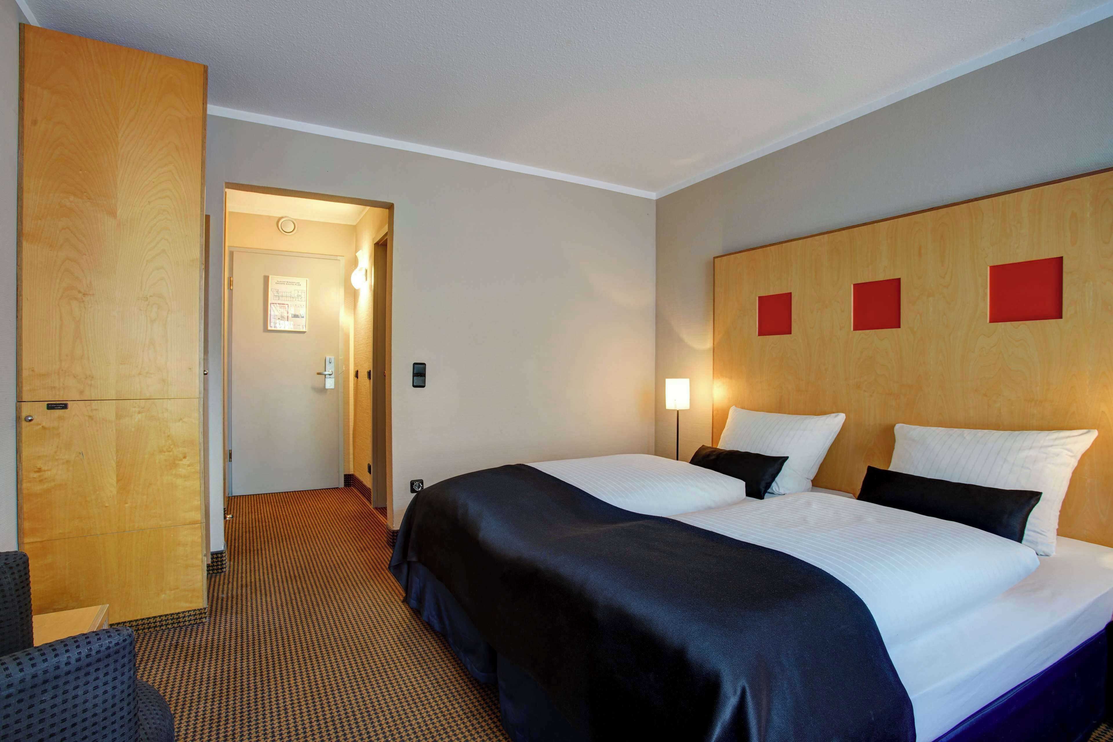 A hotel room with a large bed, a wooden wardrobe, a desk, and a chair.
