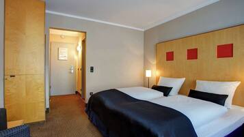 A hotel room with a large bed, a wooden wardrobe, a desk, and a chair.