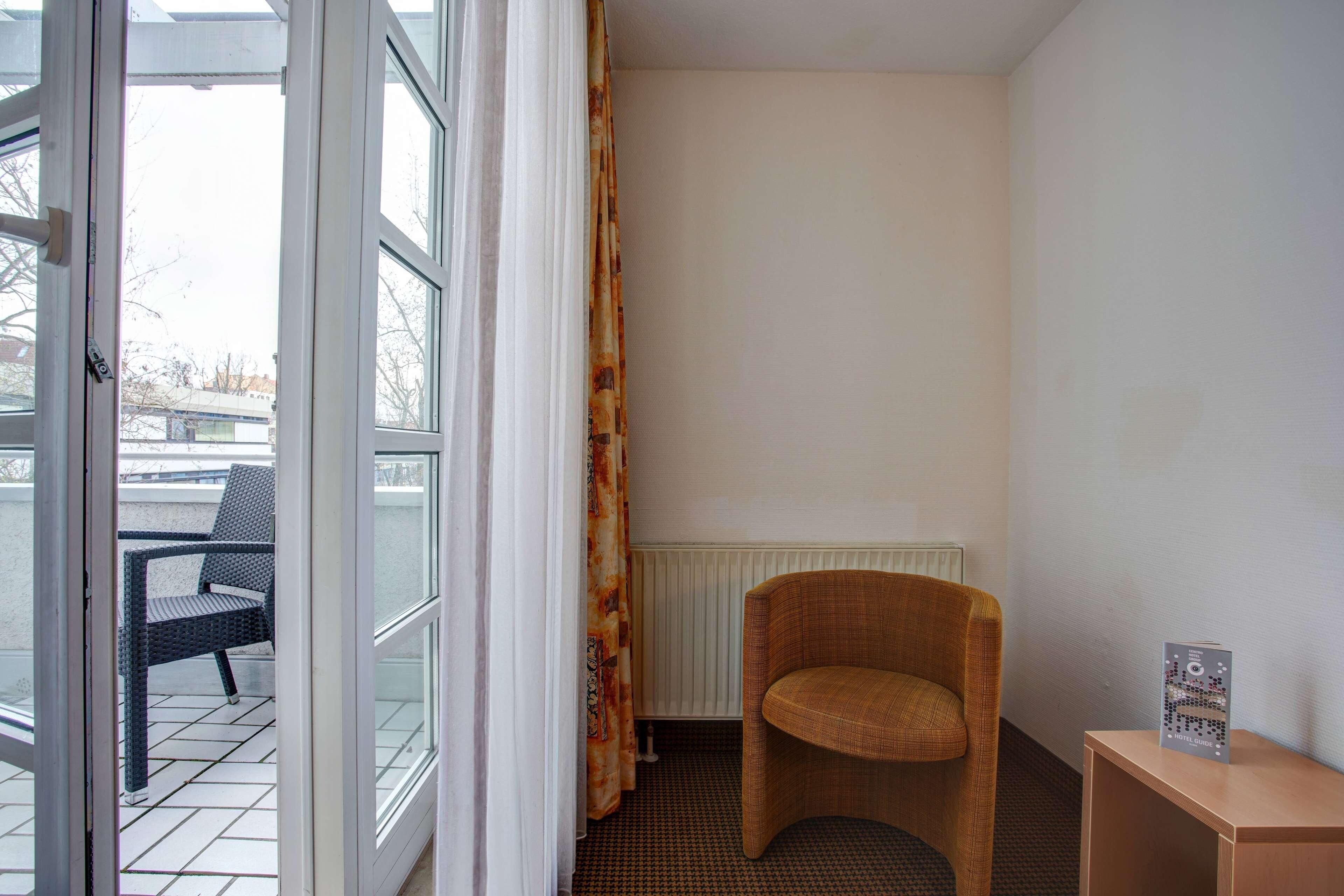 Habitación de hotel con vista al exterior, una silla, un radiador y una pequeña mesa con una guía hotelera.