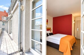 Un pasillo con ventana y cama, pared roja y manta naranja.