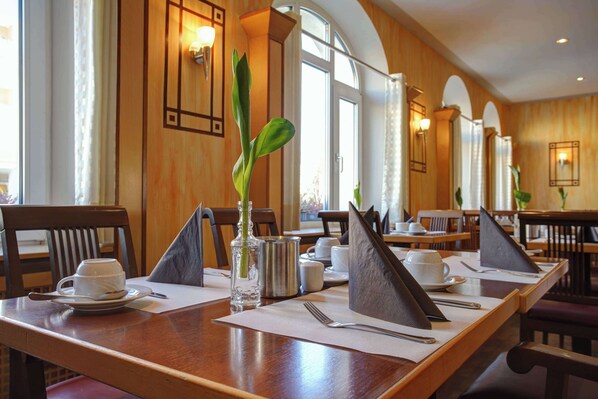 Un comedor con mesas de madera, platos blancos, cubiertos y un florero con una planta verde.