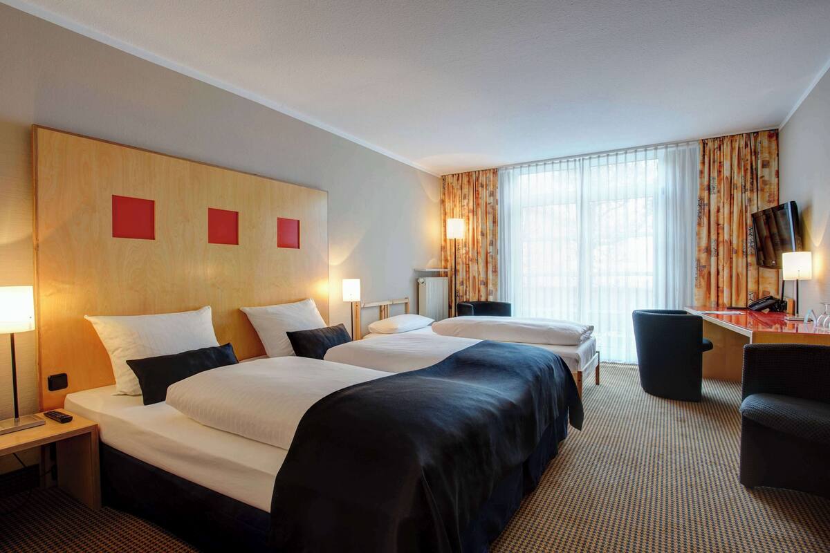 A hotel room with two beds, a desk, a chair, and a TV.