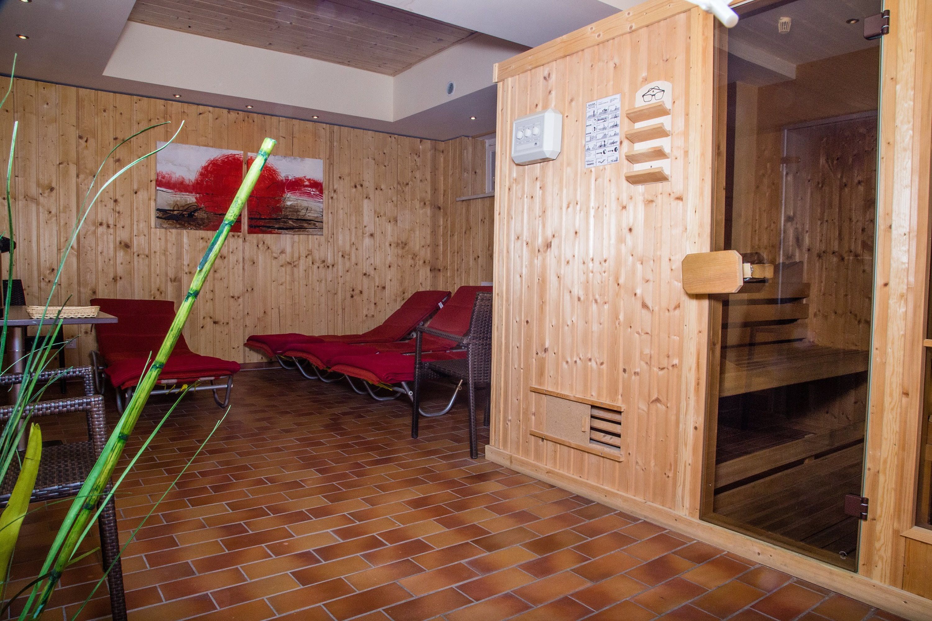 A sauna room with wooden walls, red chairs, and a tiled floor.