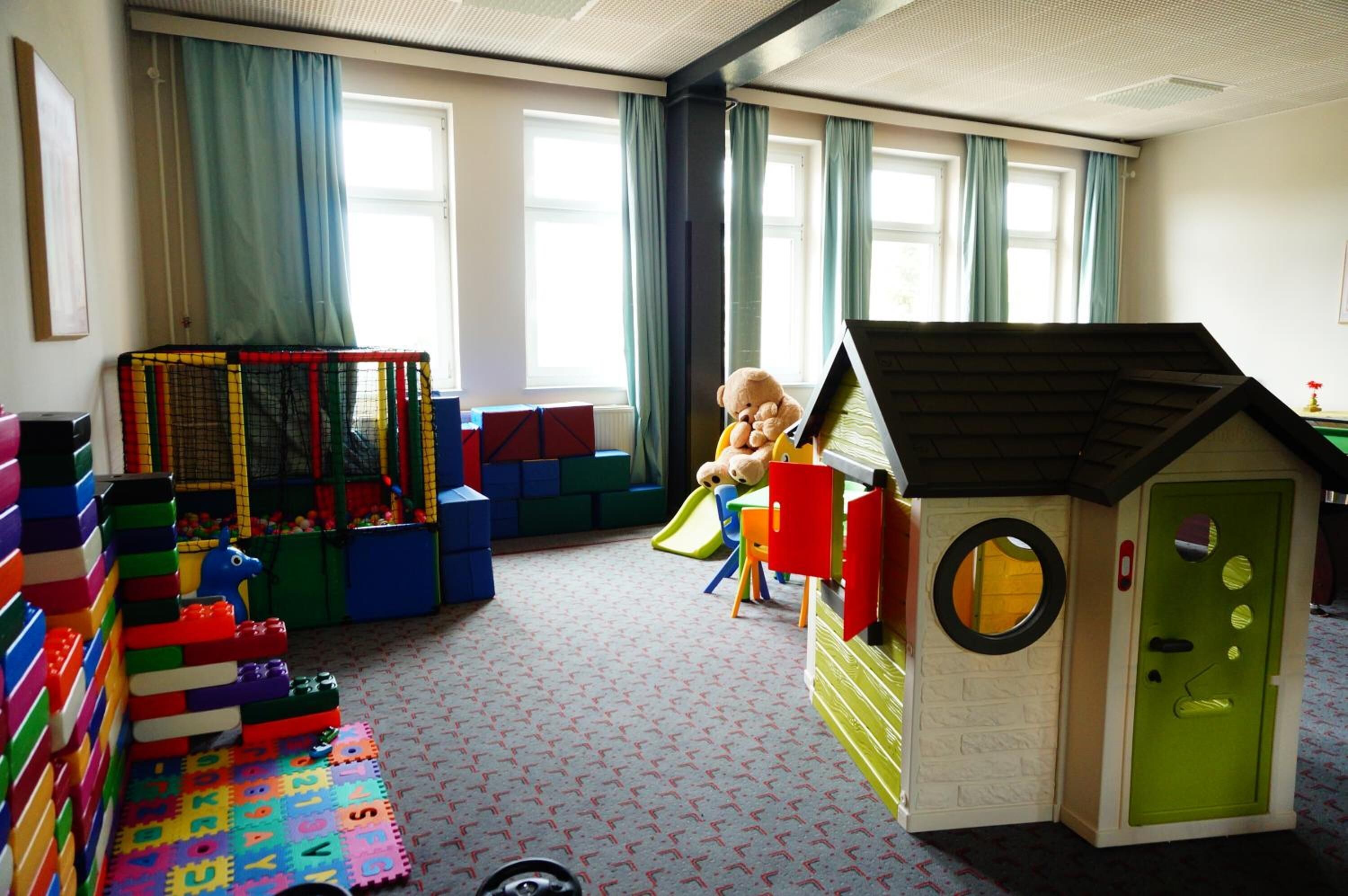 Una sala de juegos con una casita de juegos, bloques de construcción coloridos y un corralito.