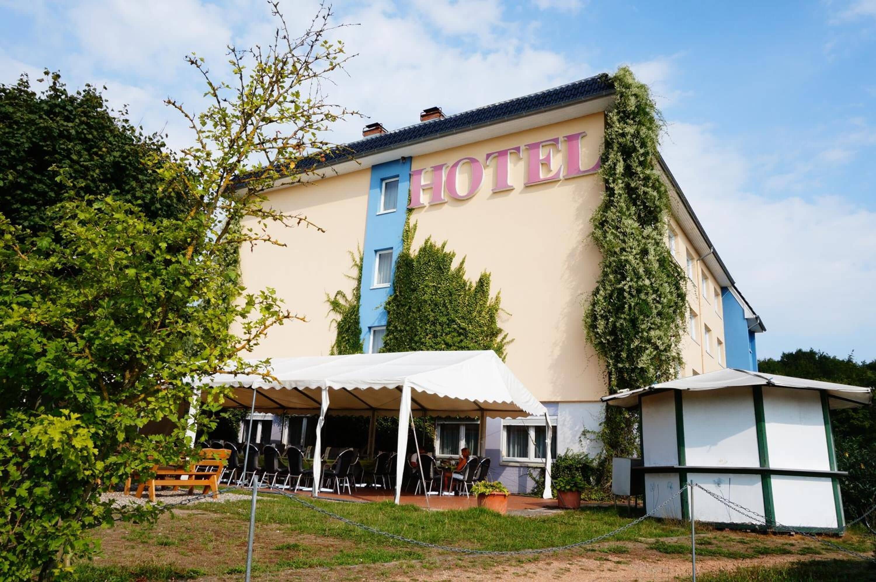 Ein Hotel mit großer Schrifttafel, Außenbestuhlung und überdachter Terrasse.