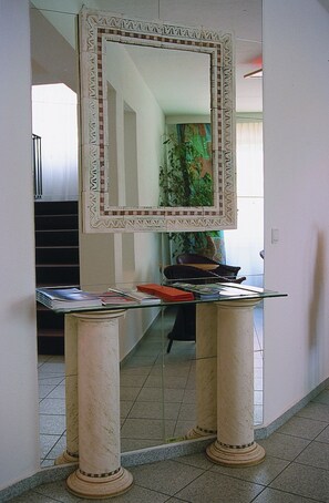 Un pasillo con un espejo decorativo sobre una mesa de vidrio, flanqueado por dos columnas.